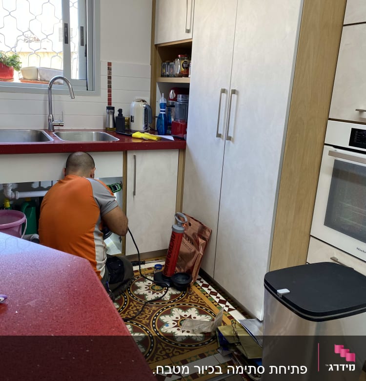 אדם עובד מתחת לכיור עם כלי עבודה.